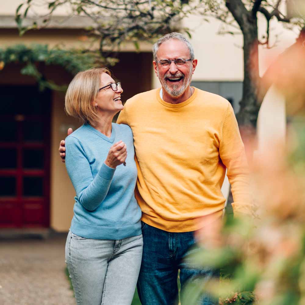 Senior couple holding keys and smiling outside their home